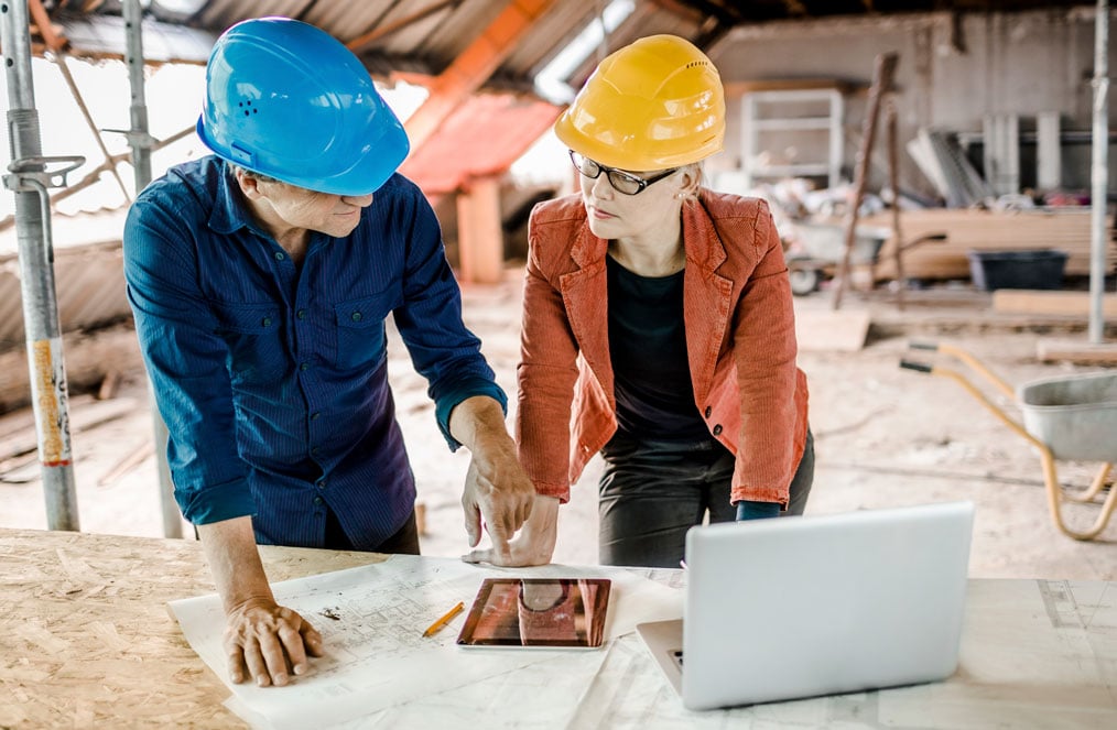 Man and woman on a construction site looking at a tablet and laptop