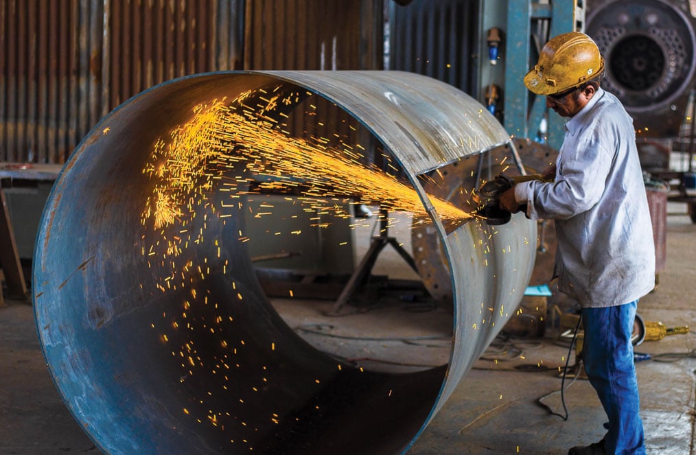 Man cutting metal cylinder with sparks flying 